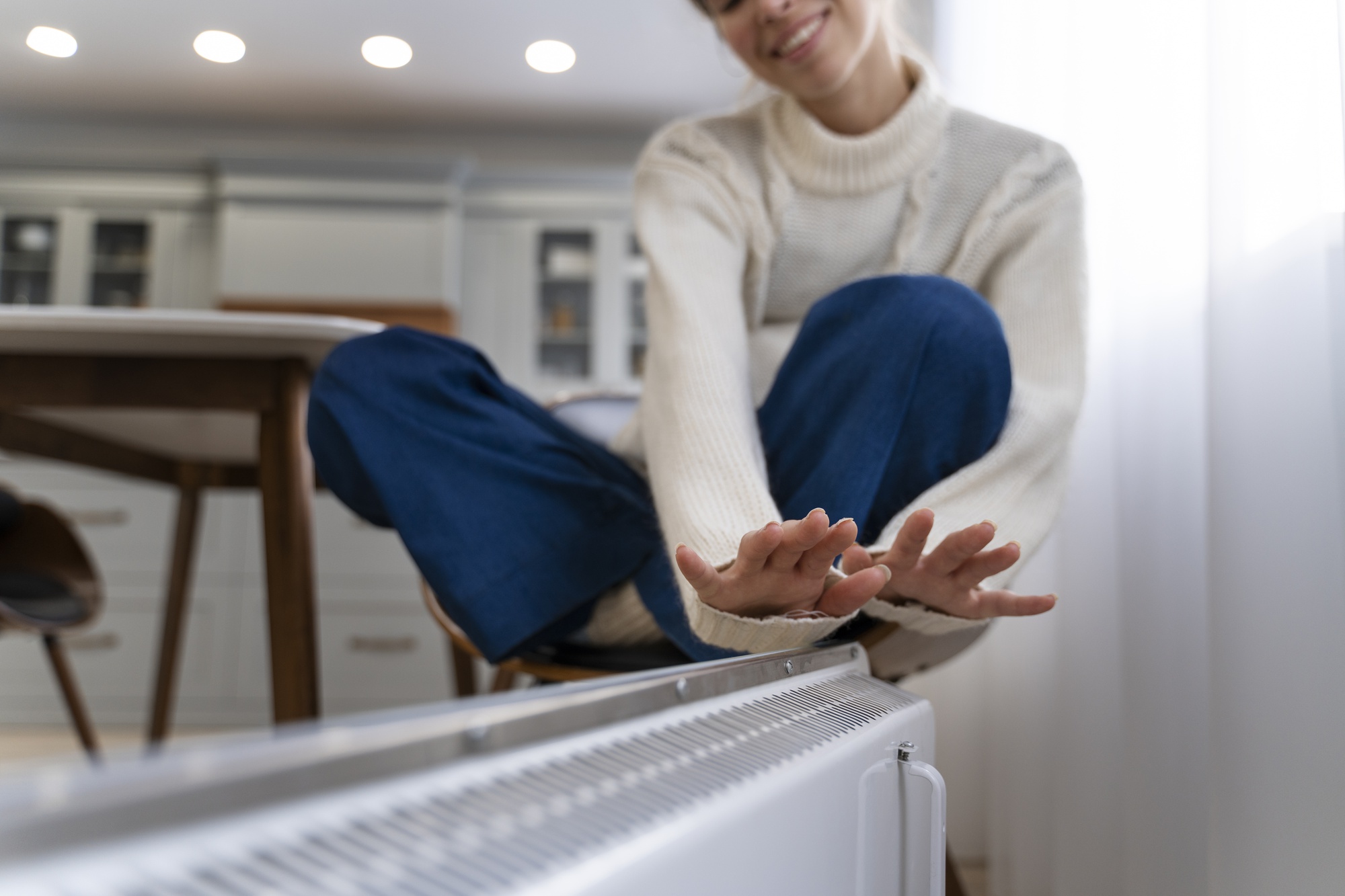 Woman warming hands near radiator heat pumps New Hampshire